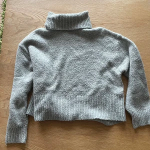 Grå polotröja i ullmix - Mysig grå polotröja med ribbade muddar och hög krage. Tröjan är stickad och har en avslappnad passform. 