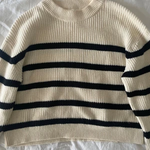 Randig stickad tröja från H&M XS - Säljer en krämvit och svart stickad tröja från H&M i storlek XS. Tröjan har breda svarta ränder, rund hals och ribbade muddar vid ärmslut och nederkant. Perfekt för dig som gillar klassisk och chill stil.