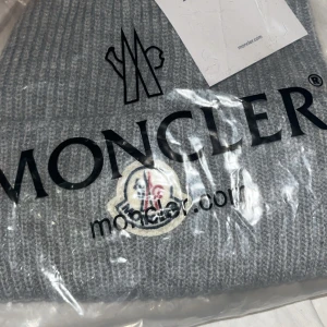 Grå stickad mössa från Moncler - Säljer en snygg grå ribbstickad mössa från Moncler med klassisk logotyp framtill. Perfekt accessoar för kyliga dagar och ger en clean look till din outfit. Mössan är tillverkad i mjukt material och har en tidlös design.