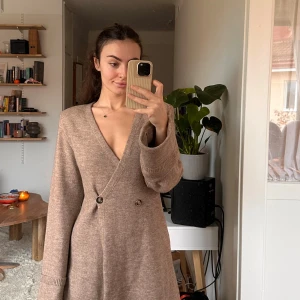 Beige stickad klänning - Superfin beige stickad klänning med omlott-design från Adoore. Aldrig använd, och har kvar prislappen. Är lite större i storleken och beroende på vilken passform man vill ha så fungerar det om man har 36-40 i storlek. Nypris 1395kr.