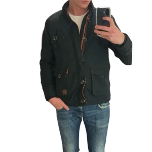 Svart jacka med knappar och fickor - Svart jacka med hög krage, stora knappar och praktiska fickor framtill. Snygga bruna detaljer vid dragkedjan och fickorna ger en cool kontrast. Jackan har en rak passform och är perfekt för dig som gillar stilren och funktionell design.