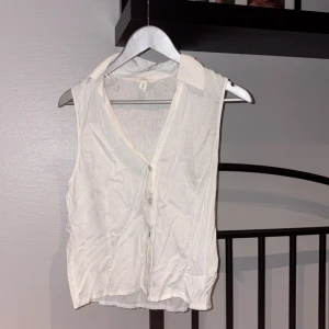Vit ärmlös linnetopp från H&M - Säljer en vit ärmlös linnetopp från H&M med klassisk krage och knäppning framtill. Toppen är i en luftig linneblandning och har en avslappnad passform, perfekt för varma dagar. Enkel och stilren design som funkar till många olika looks.