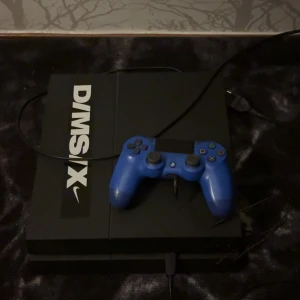 PlayStation 4 - Snygg PlayStation 4 med blå DualShock 4-kontroll. Inga synliga skador eller slitage, kablar medföljer. Perfekt för gaming och underhållning!