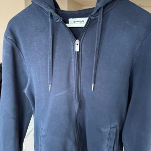 Mörkblå hoodie från Kappahl - Snygg mörkblå hoodie från Kappahl i storlek S. Tröjan har dragkedja framtill, huva med snörning och två fickor. Tillverkad i mjuk bomullsmix, perfekt för chill dagar. Långärmad och klassisk passform.