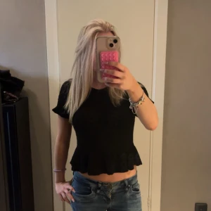 Svart topp med volangkant - Säljer en svart topp med korta ärmar och volangkant nedtill. Toppen har en rund halsringning och sitter snyggt med en lite loose passform över magen. Perfekt att styla med jeans för en chill look. Skriv innan köp!❤️