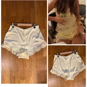 Ljusgula satinskjorts med spetskant M - Superfina ljusgula shorts i satin med dekorativ spetskant längs benen och små knappar framtill. De har en mjuk, glansig finish och en feminin vibe som passar perfekt till varma dagar. Snygg midwaist-modell med romantiska detaljer.