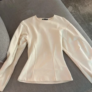 Vit långärmad blus från Zara - Säljer en stilren vit blus från Zara med lång ärm och figurnära passform. Toppen har en enkel, rund halsringning och markerade sömmar framtill som ger en snygg siluett. Perfekt för dig som gillar minimalistisk och clean stil.