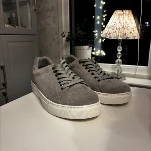 Grå mockasneakers med vit sula - Säljer dessa helt oanvända gråa sneakers av märket sandö. Finns en litet märke (se sista bild) som jag inte märkt av förens nu då jag bara haft dom i garderoben, men går förmodligen att få bort rätt så simpelt.