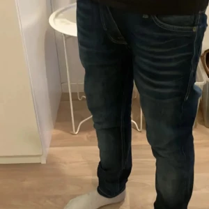 Mörkblå jeans från Jack & Jones - Snygga mörkblå jeans från Jack & Jones med klassisk femficksdesign och diskreta slitningar framtill. Jeansen har normal passform och raka ben, tillverkade i mjukt bomullsmaterial med lite stretch för extra komfort.