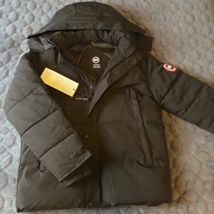 Canada Goose Jacka - Säljer en svart dunjacka från Canada Goose med huva och klassisk logga på ärmen. Jackan är quiltad, har dragkedja och knappar framtill samt två snedställda fickor. Perfekt för kalla vinterdagar och riktigt snygg streetstil. Jackan är aldrig använd och pälsen till luvan följer självklart med. Tveka inte på att höra av dig vid frågor!😁