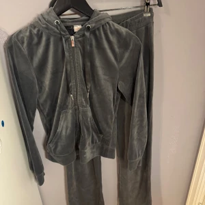 Gråa mjukisbyxor i velour med kofta - De kända mjukissettet grå i mjuk velour med dragsko i midjan. Perfekta för chill dagar hemma eller när du vill vara extra bekväm ute. Byxorna har en rak/flared passform och elastisk midja med snörning för bästa komfort. Koftan är i XS och mjukis byxorna är i S. Hela settet säljs tillsamans. Mjukissettet är i mycket fint skick och det som på bilder ser skiftande ut i färger eller ”skrynkligt ut är då det är velour och inga användningstecken. Vid intresse skickas fler bilder