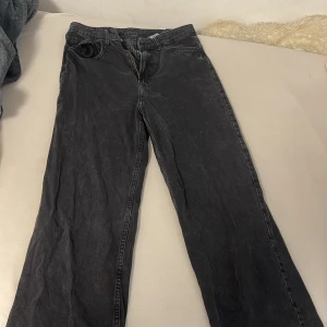 Svarta raka jeans med rå kant - Svarta jeans med rak passform och rå, fransad kant nertill. Klassisk femficksmodell med dragkedja och knapp framtill. Jeansen har en tvättad look och är tillverkade i kraftigt denimtyg. Perfekta för en avslappnad och trendig stil.