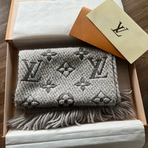Grå Louis Vuitton halsduk Logomania - Lyxig grå halsduk från Louis Vuitton med ikoniskt monogrammönster och tjock stickad struktur. Kommer med originalkartong och kvitto.