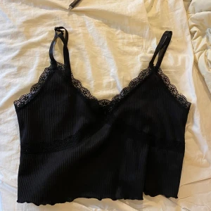 Svart croppad spetslinne från H&M Divided - Svart croppad linne från H&M Divided med tunna axelband och v-ringning. Toppen har ribbad struktur och fina spetsdetaljer längs halsringningen och under bysten. Perfekt att styla med jeans eller kjol för en trendig look. Storlek M 🖤🖤