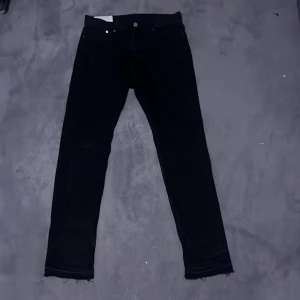 Svarta slim jeans flared jeans  från H&M - Svarta jeans från H&M i slim fit-modell med klassisk femficksdesign och råa, fransiga benslut. Jeansen har en smal passform och är tillverkade i ett mjukt bomullsmaterial med lite stretch för extra komfort. Perfekt för dig som gillar en stilren och enkel look.