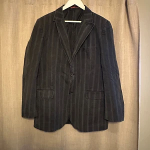 Svart randig jackkavaj från Batistini - Snygg svart kavaj från Batistini i storlek 54, tillverkad i 100% bomull. Kavajen har ett klassiskt randigt mönster, två knappar framtill och fickor med lock. Fodret är svart med röda detaljer. Perfekt för dig som gillar stilrena och tidlösa plagg.