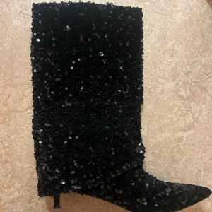 Svarta paljettstövlar med klack - Säljer dessa otroligt fina bootsen från Nelly som tyvärr inte kommer till användning! De är bara använda en gång, så är i fint skick! Det är storlek 40, jag har strl 39 men passar perfekt ändå❤️‍🔥❤️‍🔥 Nypris: 1100kr