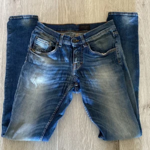Blå jeans från Tiger of Sweden - Snygga blå jeans från Tiger of Sweden med klassisk femficksdesign och slitningar framtill. Jeansen är slim fit och har orangea kontrastsömmar. Tillverkade i jeansmaterial som ger en autentisk känsla och passar perfekt till en avslappnad stil.