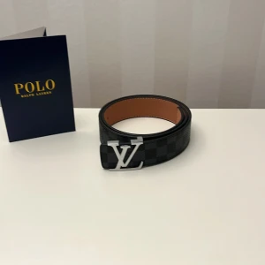  svart skinnbälte - Säljer ett stilrent  bälte i svart skinn med klassiskt rutigt mönster och ett silver som spänne. Insidan är brun med vit söm. Perfekt accessoar för dig som vill ha en lyxig och modern look.