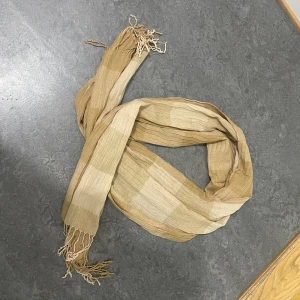 Beige rutig halsduk med fransar - Luftig och lätt halsduk i rutigt mönster med olika nyanser av beige och ljusbrun. Halsduken har tunna, vågiga ränder i tyget och avslutas med fransar i båda ändar. Perfekt accessoar för att lyfta din outfit med en naturlig och stilren look.