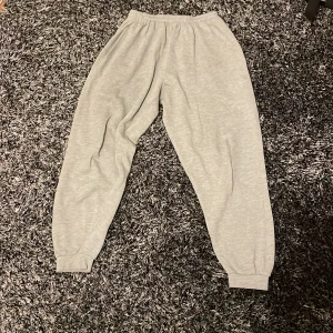 Grå mjukisbyxor från DFC, stl S - Grå mjukisbyxor från DFC i storlek S. Byxorna har resår i midjan och vid bensluten för en skön och avslappnad passform. Tillverkade i mjukt bomullsmaterial som är perfekt för chill dagar eller när du vill vara bekväm.