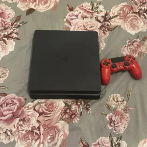 PlayStation 4 Slim - Sony PlayStation 4 Slim med en röd DualShock 4-kontroll. Konsolen är i gott skick med mindre ytliga repor, inga synliga större skador. Perfekt för gaming och multimedia. Kontrollens knappar och styrspakar ser hela ut.