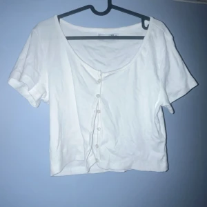 Vit croppad kofta från 157 - Säljer en vit croppad kofta från 157 med korta ärmar och rundad hals. Koftan har knappar framtill och är gjord i mjuk bomull, perfekt för dig som gillar enkel och clean stil. Passar dig som vill ha en chill och snygg look.