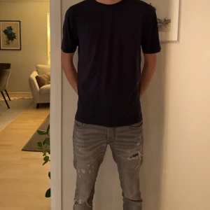 Blå t-shirt från East West, storlek L - En stilren blå t-shirt från East West i storlek L. Modellen är klassisk med rund hals och korta ärmar, perfekt för en clean och enkel look. Materialet är mjukt och känns skönt mot huden, troligtvis bomull. Passformen är normal och funkar till de flesta outfits.