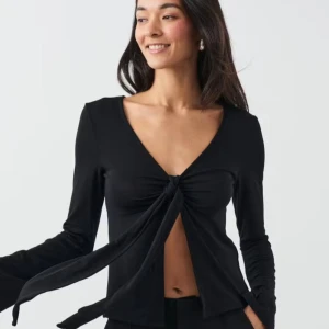 Svart långärmad topp med knyt Gina Tricot - Helt oanvänd svart långärmad topp från Gina Tricot med djup v-ringning och snygg knytning framtill. Tunn och mjuk i materialet, perfekt till jeans eller kjol. Enkel och stilren design som ger en trendig look🖤