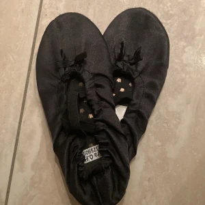 Svarta ballerinaskor från H&M strl 32/33 - Svarta ballerinaskor från H&M i storlek 32/33. Skorna har elastiskt band över foten för extra passform och en liten rosett framtill. Ytan är i glansig textil och innersulan är ljusgrå. Perfekta för dans eller som inneskor.