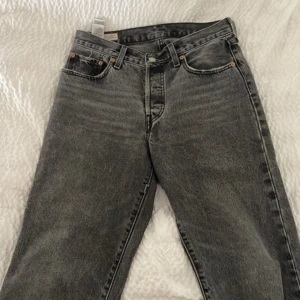 Levi's Premium svarta jeans W26 L30 - Snygga svarta Levi's Premium jeans i klassisk rak modell. Jeansen har fem fickor, bälteshällor och knappgylf. Materialet är robust denim i bomull och färgen är tvättad svart med vintagekänsla. Perfekta för dig som gillar tidlös stil.