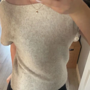 Beige stickad topp  - Snygg beige stickad topp med korta ärmar från Nelly . Tröjan har en snygg och unik sne passform upprop om man vill ha den hängandes på axeln lite. Enkel och stilren design som passar till många olika outfits.