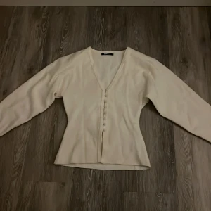 Beige blus med v-ringning från Gina Tricot - Säljer en stilren beige blus från Gina Tricot i storlek XS. Blusen har v-ringning, långa ärmar och dekorativa knappar framtill. Säljer då den aldrig kommer till användning. Endast använd 1 gång och har inga defekter alls.