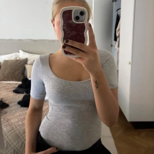 Ljusgrå ribbad body med kort ärm - Säljer en ljusgrå ribbad body med korta ärmar och rundad halsringning. Toppen har en slim passform och är tillverkad i mjuk bomull som sitter skönt mot kroppen. Perfekt att styla med jeans eller kjol för en enkel och fräsch look.