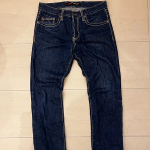 Mörkblå jeans från Cipo & Baxx - Ett par riktigt feta jeans från Cipo & Baxx med kontrasterande vita sömmar och en otvättad look🙌. Jeansen har raka ben och tydliga detaljer på bakfickorna. Perfekt för dig som gillar en stilren och modern look!