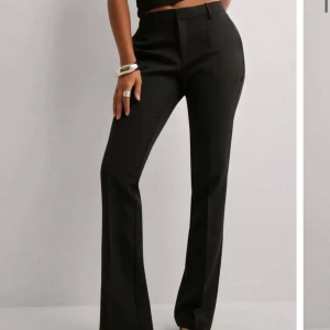 Bikbok vilma - Snygga svarta kostymbyxor med bootcut-silhuett och hög midja. Byxorna har klassiska pressveck, hällor för bälte och fuskfickor bak. Perfekta för en clean och stilren look. Materialet är slätt och känns dressat.
