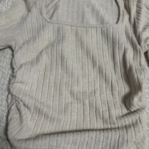 Beige ribbad topp med fyrkantig ringning - Säljer en beige ribbad topp med fyrkantig ringning och rynkade sidor. Toppen har korta ärmar och är tillverkad i ett mjukt, stretchigt material som känns skönt mot huden. Perfekt för dig som gillar en enkel men trendig look.