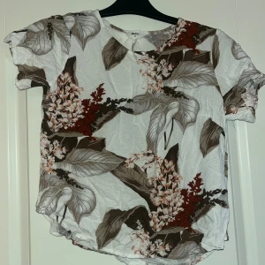 Blommig blus från Object, strl 34 - Säljer en snygg blus från Object i storlek 34. Blusen är vit med stora blommiga mönster i brunt och rött, har rund hals och korta ärmar. Materialet är lätt och luftigt, perfekt för varmare dagar. Passar dig som gillar naturinspirerade prints och relaxed vibe. Är en XS men tycker den är liten i storlek 
