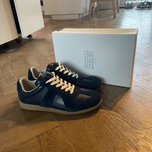 Maison margiela skor - Snygga mörkblå sneakers med ovandel i skinn och mocka, vita snören och klassisk gummisula. Skorna har en stilren och sportig look som passar perfekt till jeans eller casual outfits.