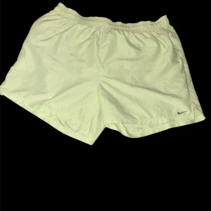 Ljusgula Nike shorts med snörning - Säljer ett par ljusgula Nike shorts med elastisk midja och snörning. De har en klassisk loose fit och är perfekta för träning eller chill dagar. Materialet är lätt och känns svalt mot huden. Diskret Nike-logga broderad på benet.