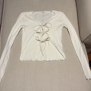 Vit ribbad blus med snörning från nelly - Supersöt vit blus i ribbat material med långa ärmar och snygg snörning framtill. Använd några fåtal gånger. 