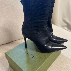 Svarta stövletter från Gucci i skinn - Säljer ett par svarta stövletter från Gucci i äkta skinn med spetsig tå och hög klack. Snygga snörningsdetaljer längs skaftet ger en edgy vibe. Perfekta för dig som vill sticka ut med lyxiga boots från ett ikoniskt märke.