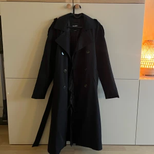 Svart trenchcoat från Pull&Bear - Svart trenchcoat från Pull&Bear med bälte i midjan. Använd ett fåtal gånger, är i fint skick! Köpt för 599 kr. 🥰