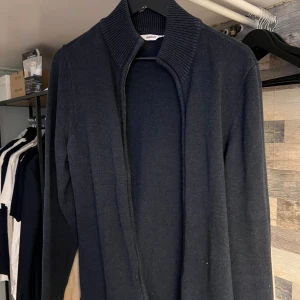 Mörkgrå stickad kofta från Dobber - Mörkgrå stickad kofta från Dobber med hög krage. Tröjan är lite tjockare och perfekt nu till vintern. Den är i storlek M