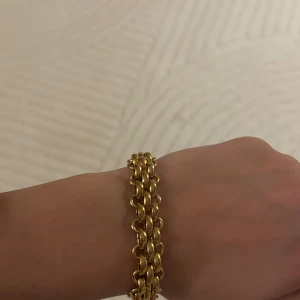 Bred guldlänk armband - Snyggt och chunky armband i guldfärgad metall med breda länkar som ger en cool och lyxig vibe. Perfekt för dig som gillar statement-smycken och vill ha något som verkligen syns på handleden. Länkarna är rundade och sitter tätt ihop för en exklusiv look.