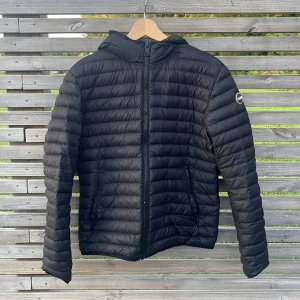 Svart Colmar Dunjacka med huva - Säljer en svart  lätt dunjacka från Colmar med huva. Har används två vinterhöstsäsgonger. Perfekt för hösten men går också utmärkt att ha på vintern. Två fickor och en innerficka. Jackan är i nästintill pedagogisk skick utan något slitage. Bara att skriva vid frågor!