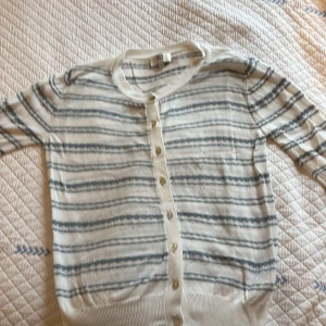 Randig kofta från Noa Noa, vit/blå S - Superfin tunnstickad kofta från Noa Noa i storlek S. Vit botten med blåa ränder, rund halsringning och knappar framtill. Långärmad och perfekt för lager-på-lager. Bra skick. Snygg till jeans eller kjol för en chill look. Köparen står för frakt❤️