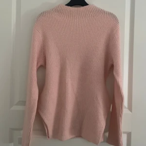 Ljusrosa stickad tröja med slits - Mysig ljusrosa stickad tröja med lång ärm och ribbad struktur. Tröjan har en liten slits i sidan 🩷
