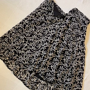 Svartvit mönstrad kjol från Joy - Fladdrig svart kjol från Joy i storlek 40 med vitt abstrakt mönster. Kjolen är lång och har ett tunt, lätt material med innerfoder. Perfekt för dig som gillar flowiga vibes och snygga prints.