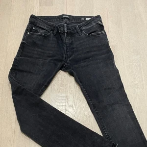 Replay jeans - Svarta jeans från Replay i modellen DOMINIQLI. Snygg, tight passform med klassisk femficksdesign och diskreta detaljer. Jeansen har svarta sömmar och en stilren läderpatch bak i midjan. Perfekta för dig som gillar en slimmad look.